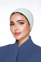 Woman wearing a light green headscarf and blue outfit against a white background