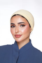 Woman wearing a beige headscarf and blue outfit on a white background
