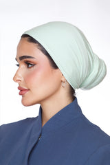 Woman wearing a light green headscarf and blue outfit on a white background