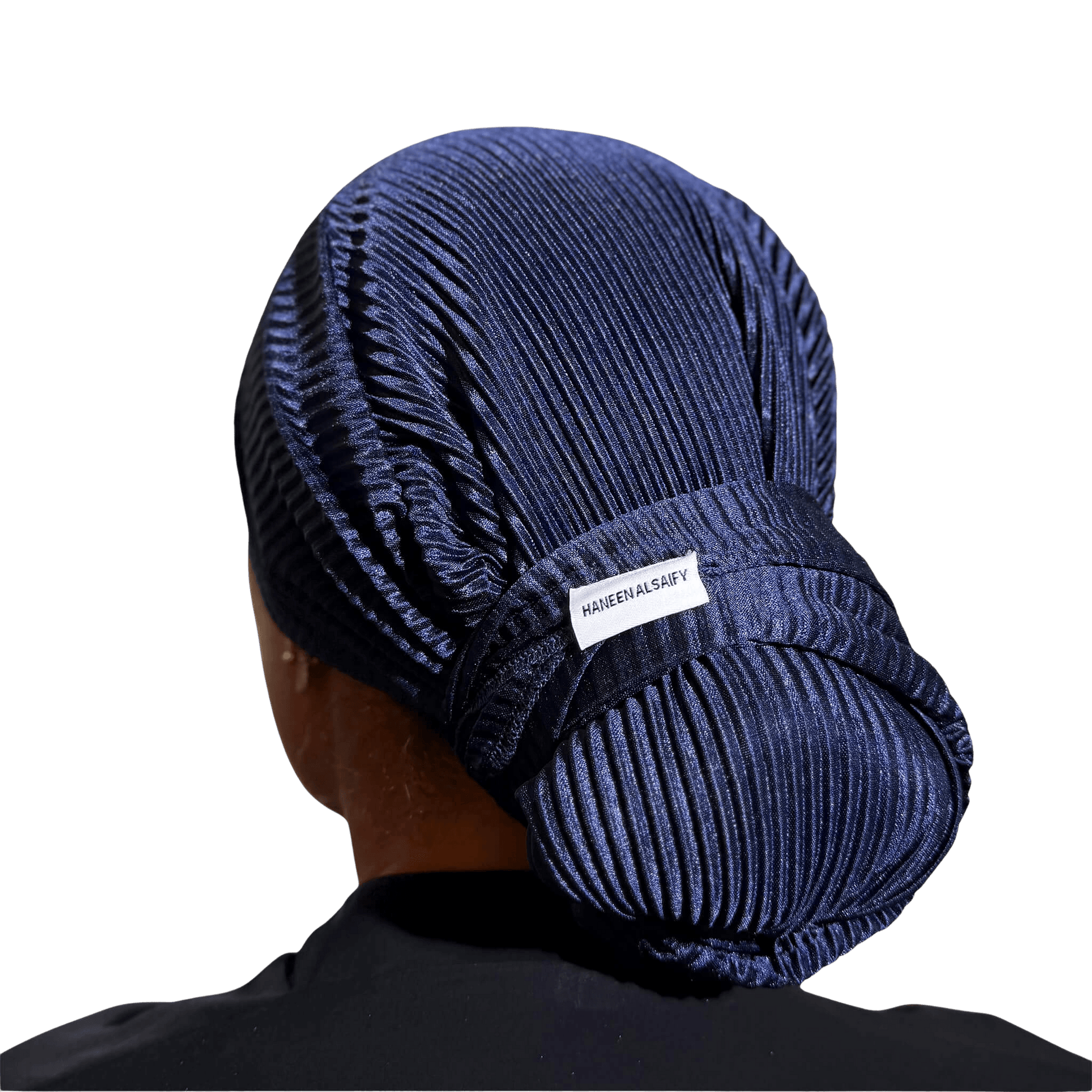 A person shown from the back wearing a dark navy pleated fabric head covering or wig cap, with a small white label reading 'HABITBANDY' visible near the back. The background is solid black.