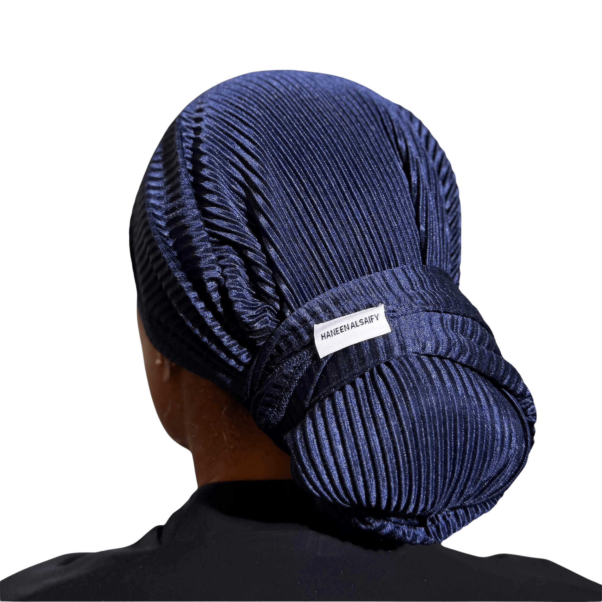 A person shown from the back wearing a dark navy pleated fabric head covering or wig cap, with a small white label reading 'HABITBANDY' visible near the back. The background is solid black.