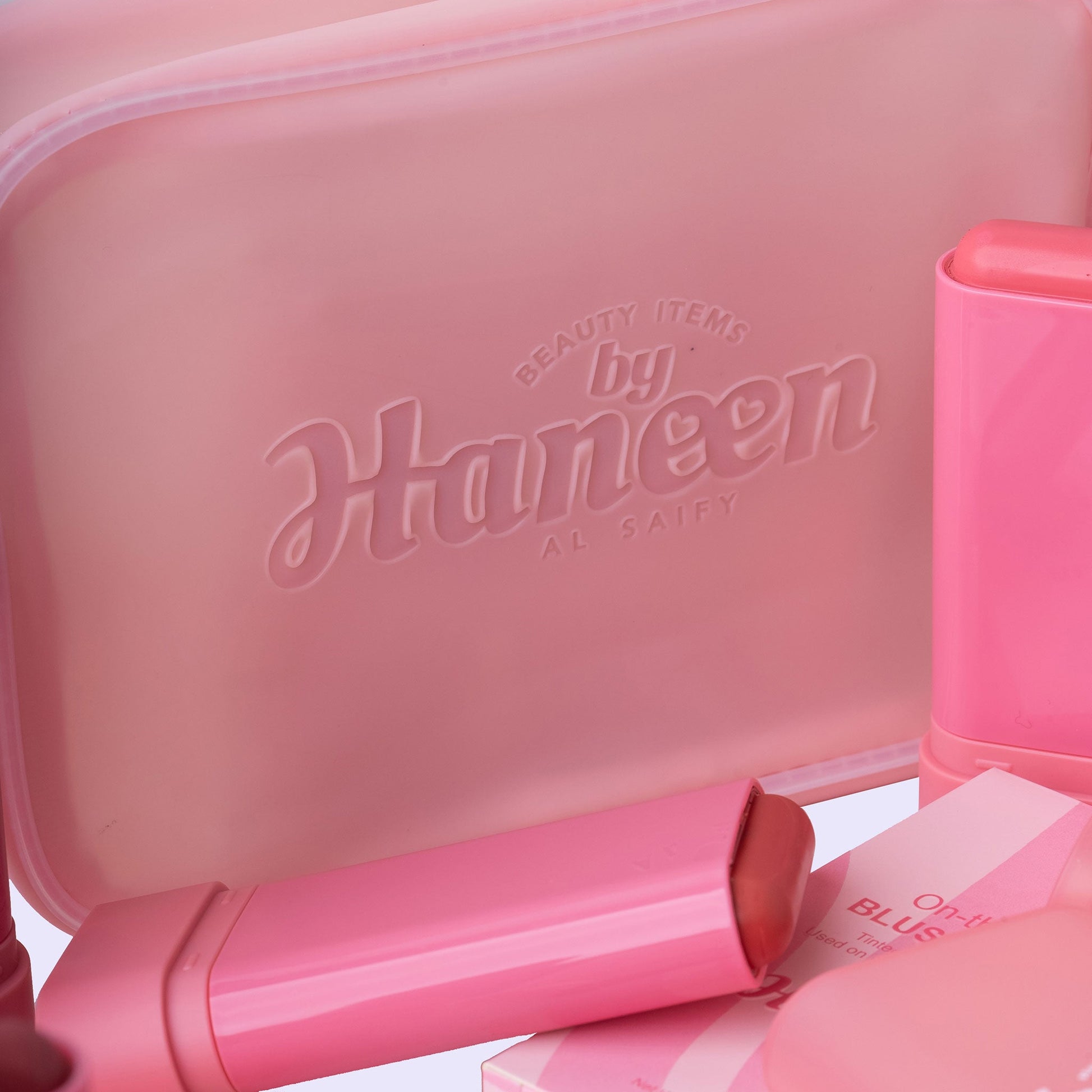 Pink cosmetic case with 'Haneen' branding and lip products on a light pink background