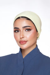 Woman wearing a beige headscarf and blue outfit against a white background