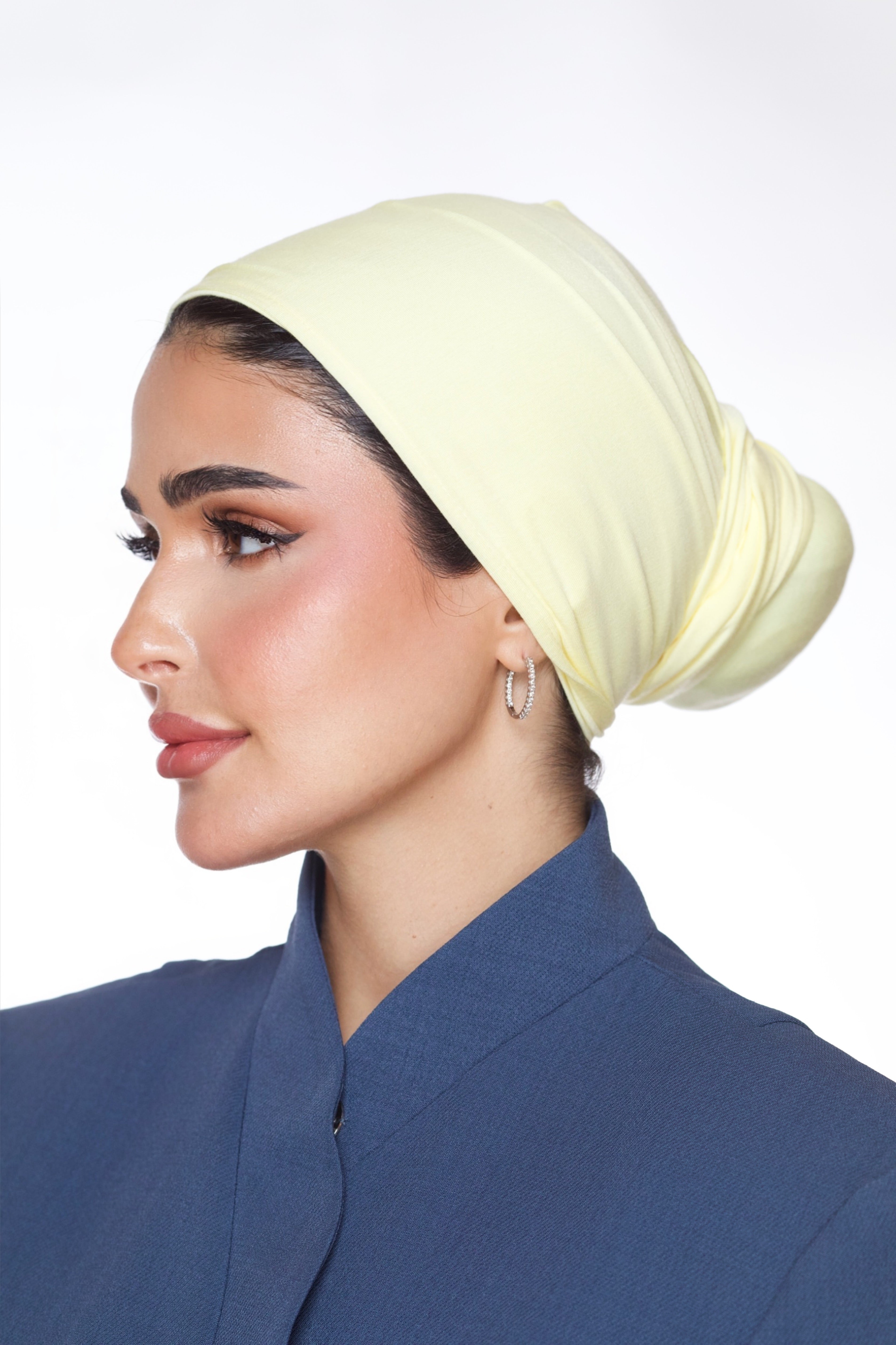 Woman wearing a light yellow headscarf and blue outfit on a white background
