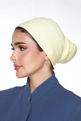 Woman wearing a light yellow headscarf and blue outfit on a white background