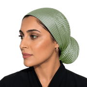 A woman shown in profile wearing a textured sage green head covering, photographed against a solid black background.