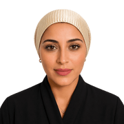 A woman wearing a cream-colored pleated hijab and a black collared garment, photographed against a solid black background.