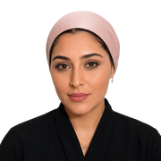 A woman wearing a light pink pleated head covering and a black abaya, shown from the chest up against a plain white background.