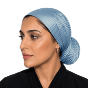 A woman shown in profile wearing a light blue textured fabric head covering or hijab against a solid black background.